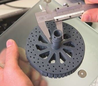 Teacher using calipers to measure the accuracy of a 3D-printed gear with design software in the background