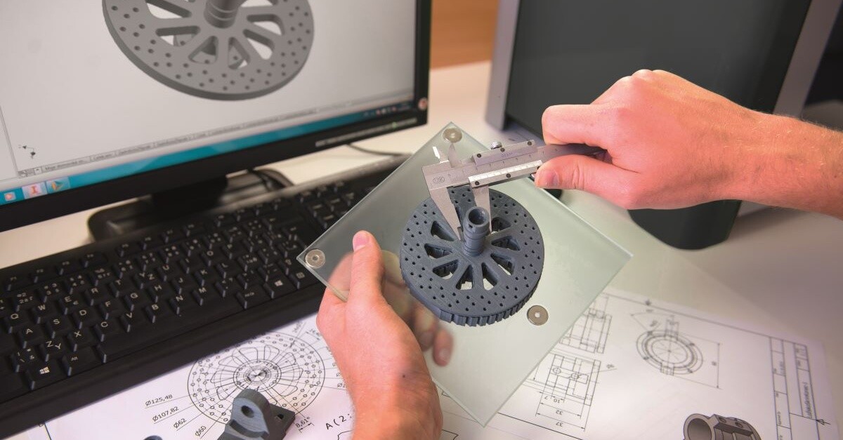 Teacher using calipers to measure the accuracy of a 3D-printed gear with design software in the background
